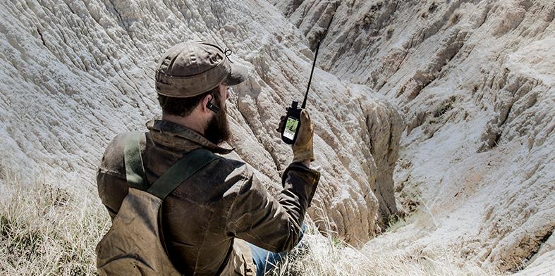 man sitting in vast wilderness looking at TEK 2.0 handheld screen